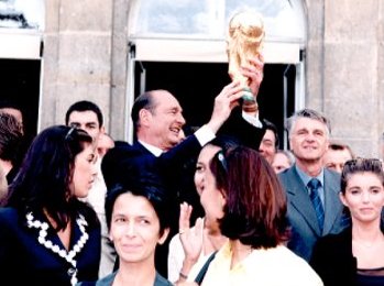 Jacques Chirac schwenkt den Weltmeisterschaftspokal im Beisein von Aimé Jacquetund den Spielern der französischen Fußballnationalmannschaft.